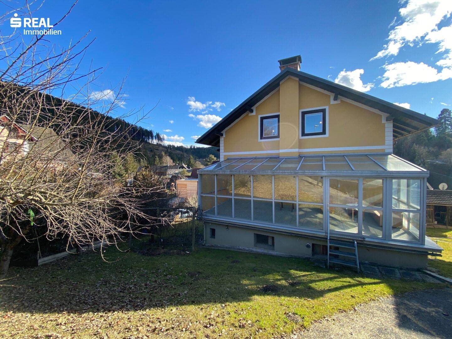 Seitenansicht des Hauses mit einem großen Wintergarten und Blick auf die umliegende Landschaft.