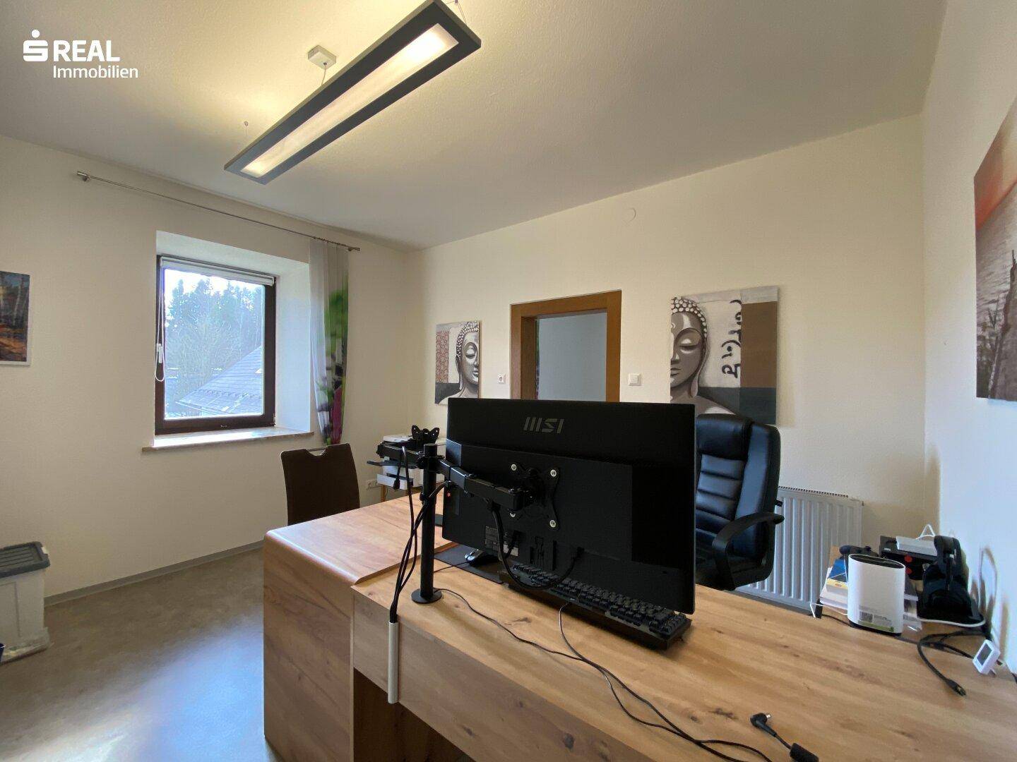 Helles Büro mit modernem Schreibtisch, Computer und Blick ins Grüne durch das Fenster.
