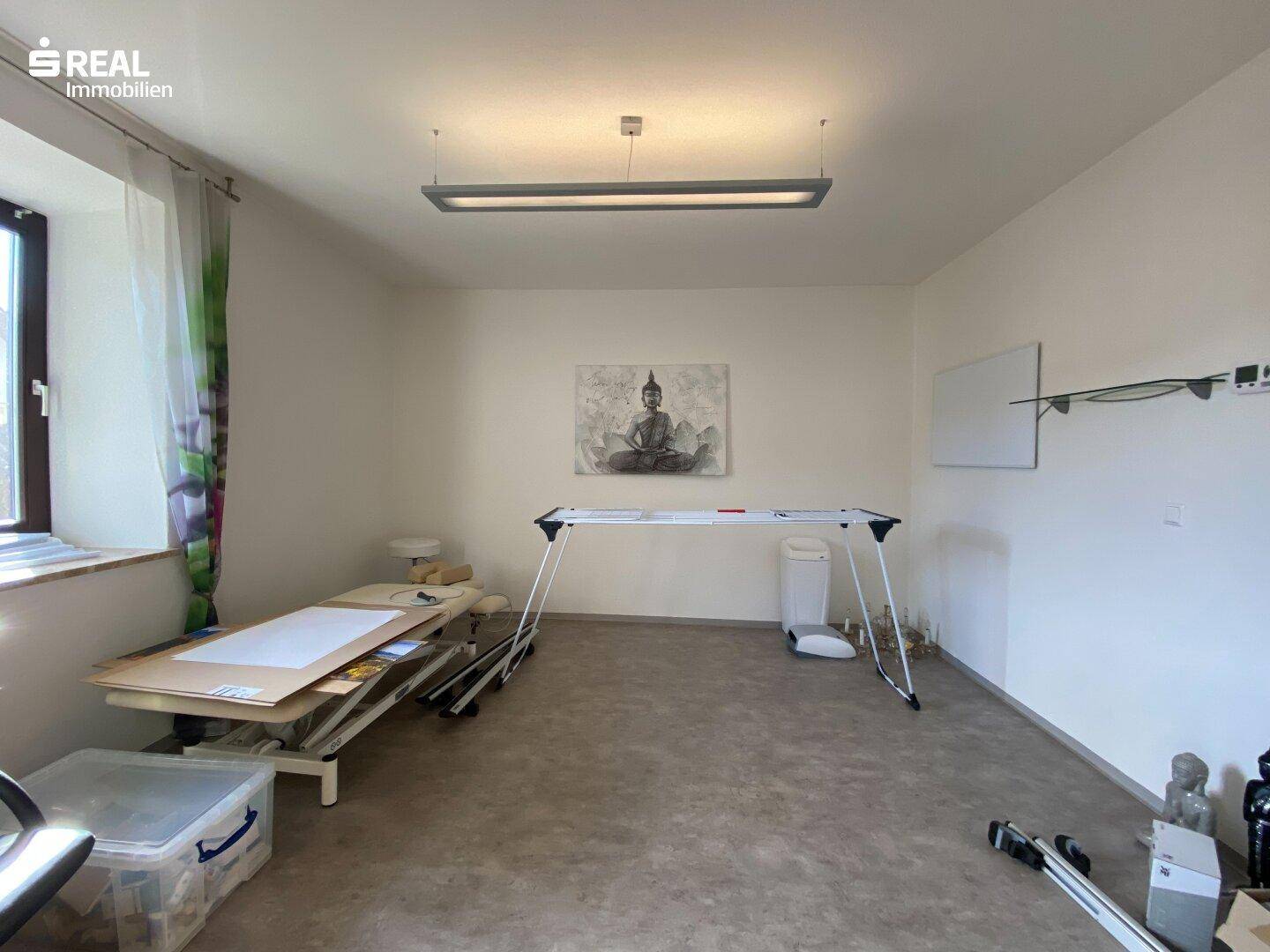 Geräumiger Raum mit hellem Boden, einem Massagetisch und minimalistischer Dekoration.