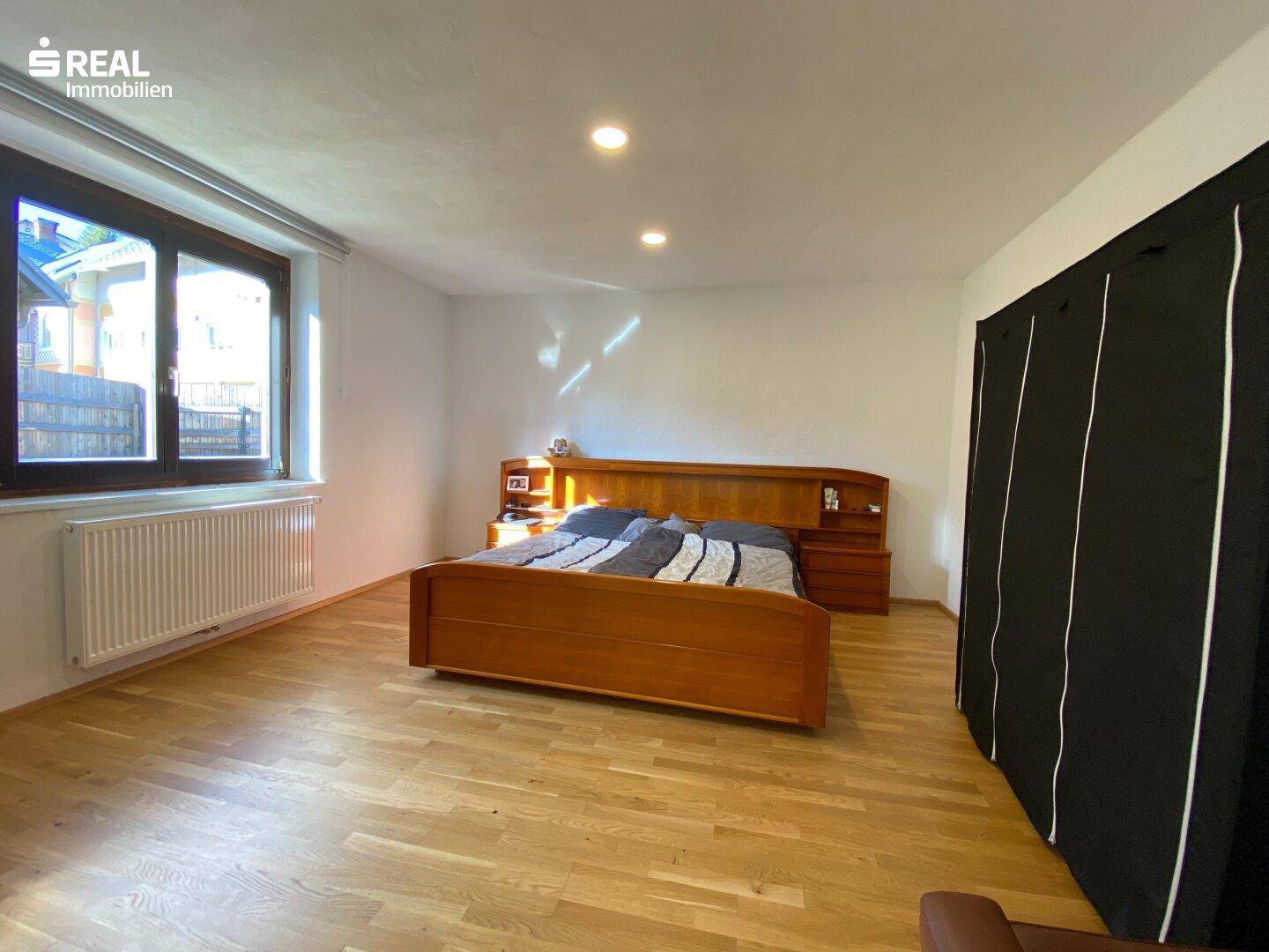 Helles Schlafzimmer mit Holzbett, Parkettboden und großem Fenster für viel Tageslicht.