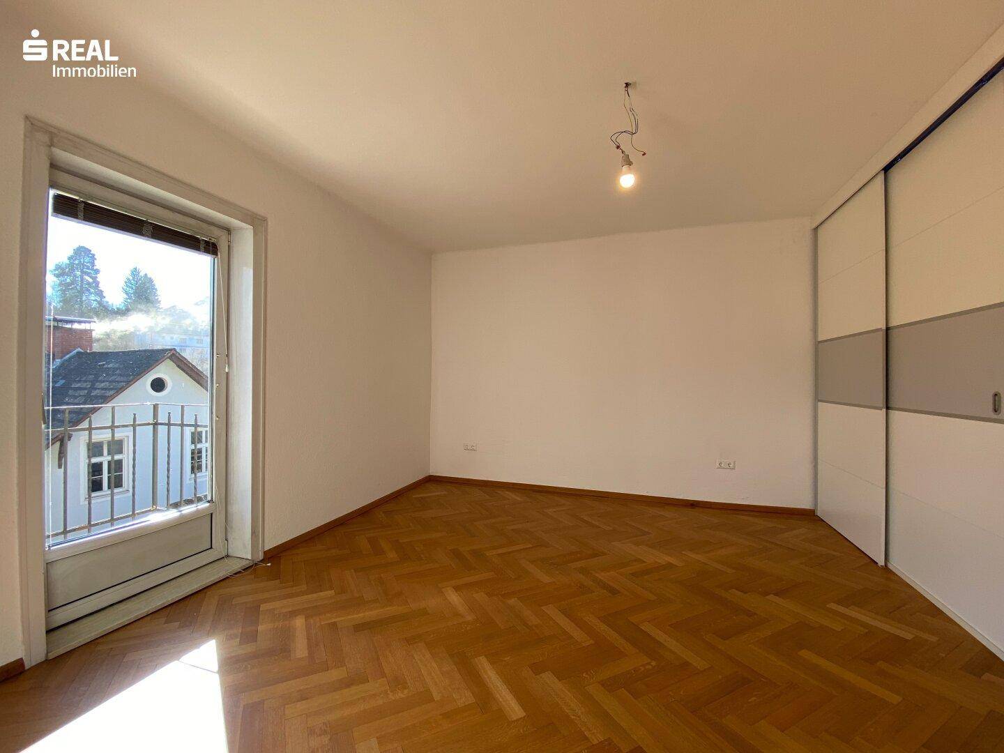 Geräumiges Zimmer mit Parkettboden, Schiebetürenschrank und Zugang zu einem französischen Balkon.