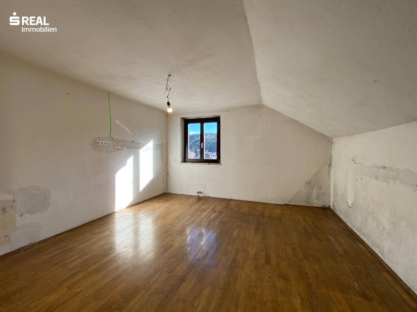 Heller Dachgeschossraum mit Holzboden, schrägen Wänden und sichtbarem Renovierungsbedarf.