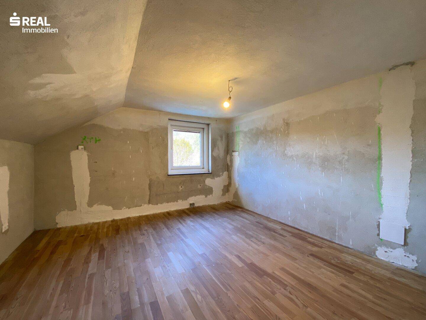 Weiterer Dachgeschossraum mit Holzboden und schrägen Wänden, bereit für den Ausbau.