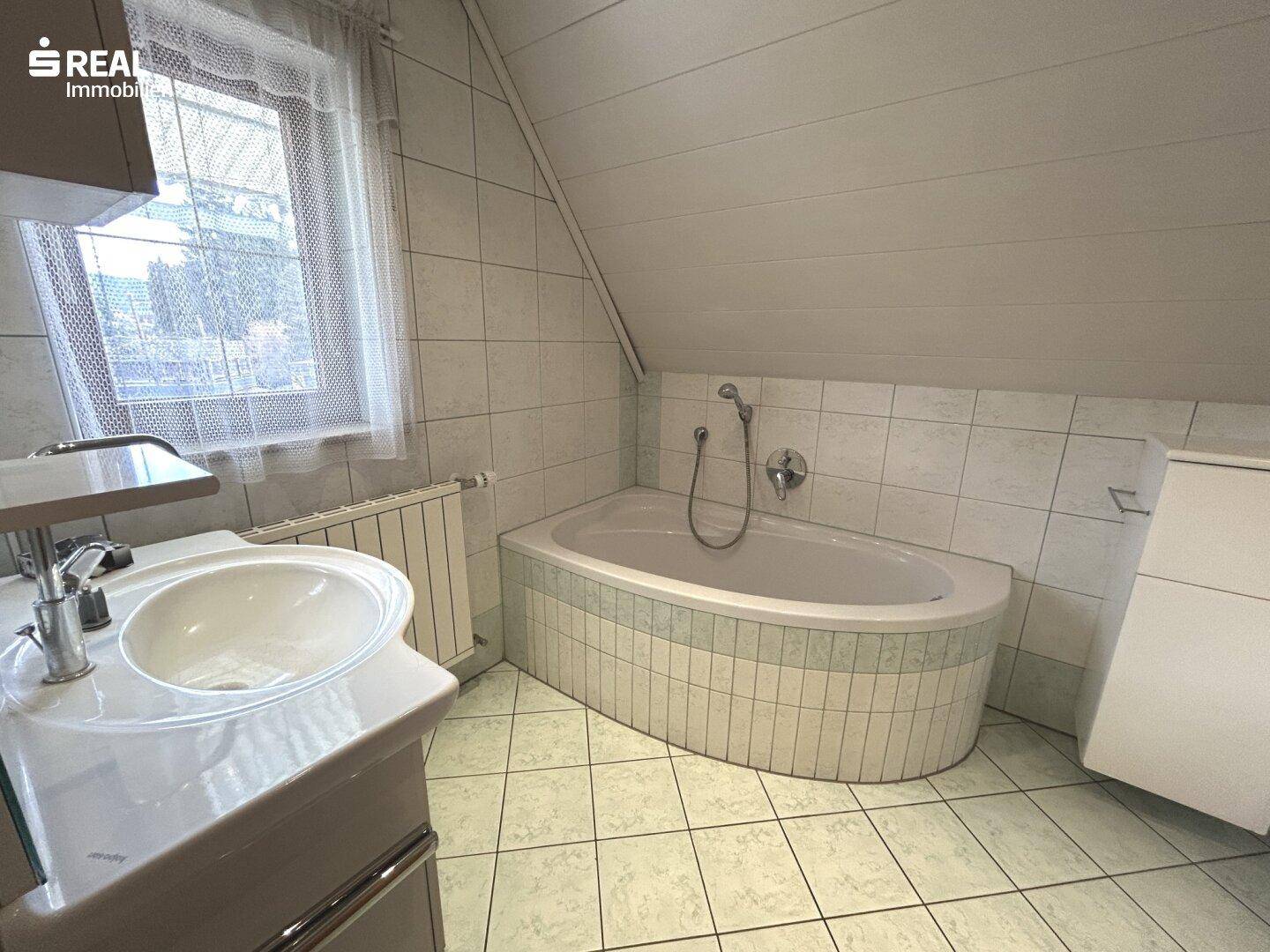 Badezimmer im Dachgeschoss mit Eckbadewanne, Waschbecken und Fliesenboden.