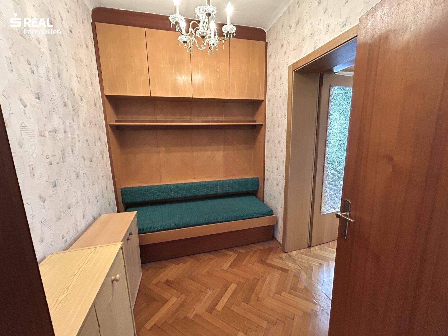 Kleines Zimmer mit Schlafsofa, Einbauschrank und Parkettboden.