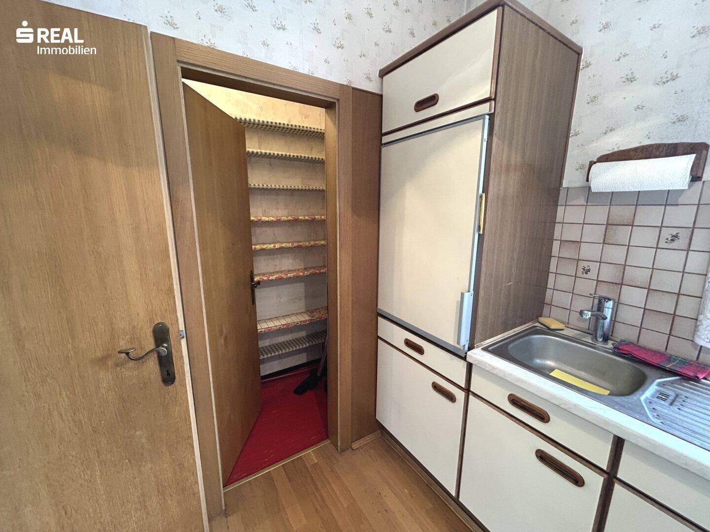 Küchenbereich mit integriertem Kühlschrank und Zugang zu einer Speisekammer.
