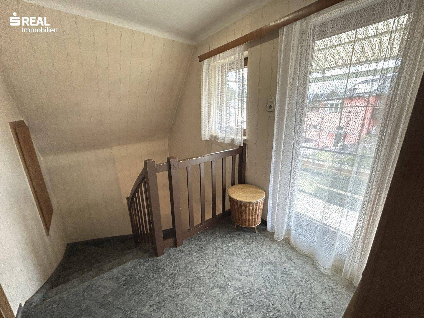 Treppenabsatz mit Teppichboden, Holzgeländer und Fenster für natürliches Licht.