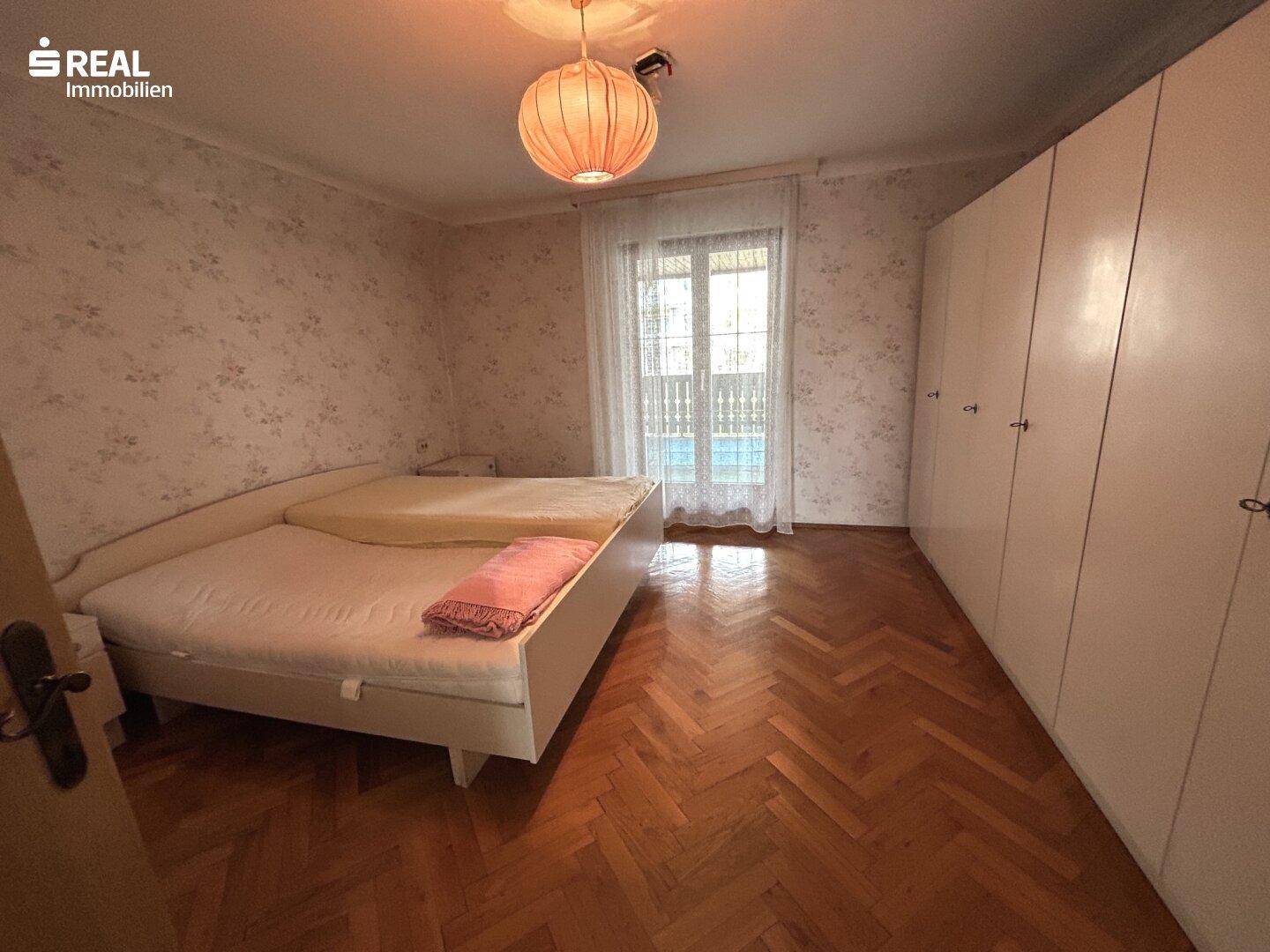Geräumiges Schlafzimmer mit Parkettboden, großen Fenstern und Zugang zum Balkon.