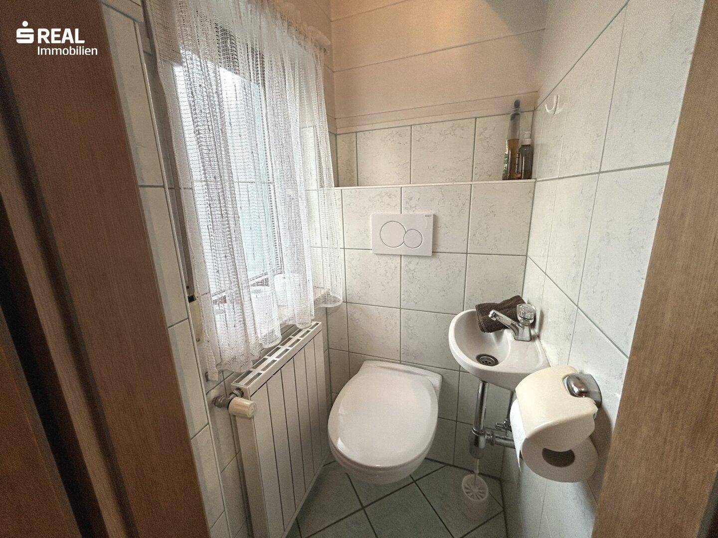 Separate Gästetoilette mit Fenster, WC und kleinem Handwaschbecken.