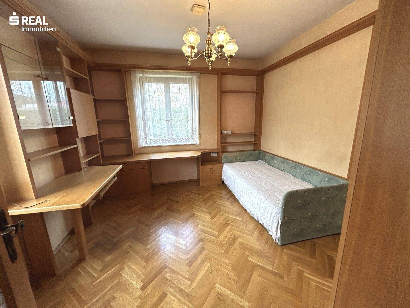 Schlafzimmer mit Holzparkett, Einbauregalen und einem Einzelbett.