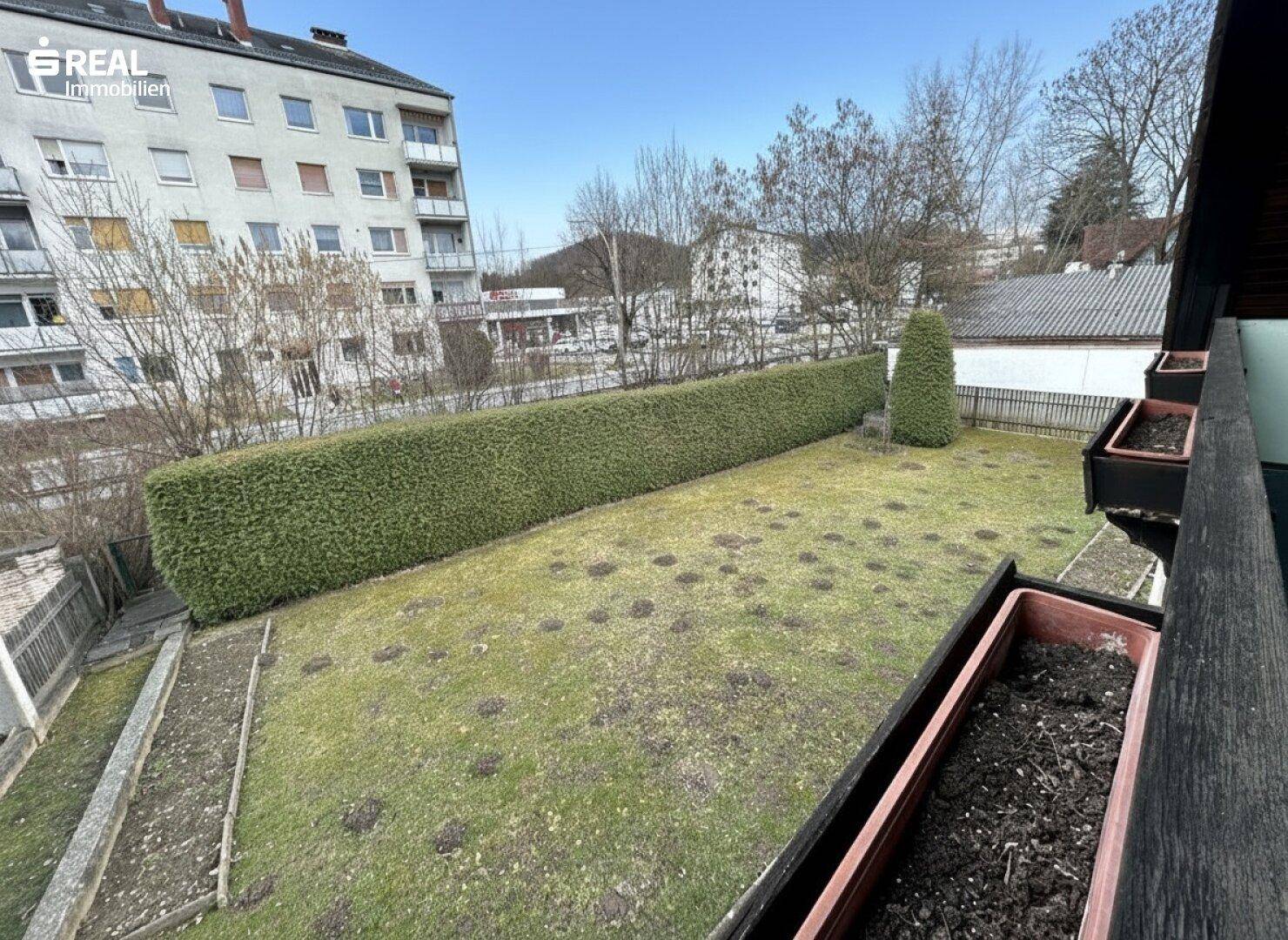 Blick vom Balkon auf den gepflegten Garten mit Hecke und Rasenfläche.