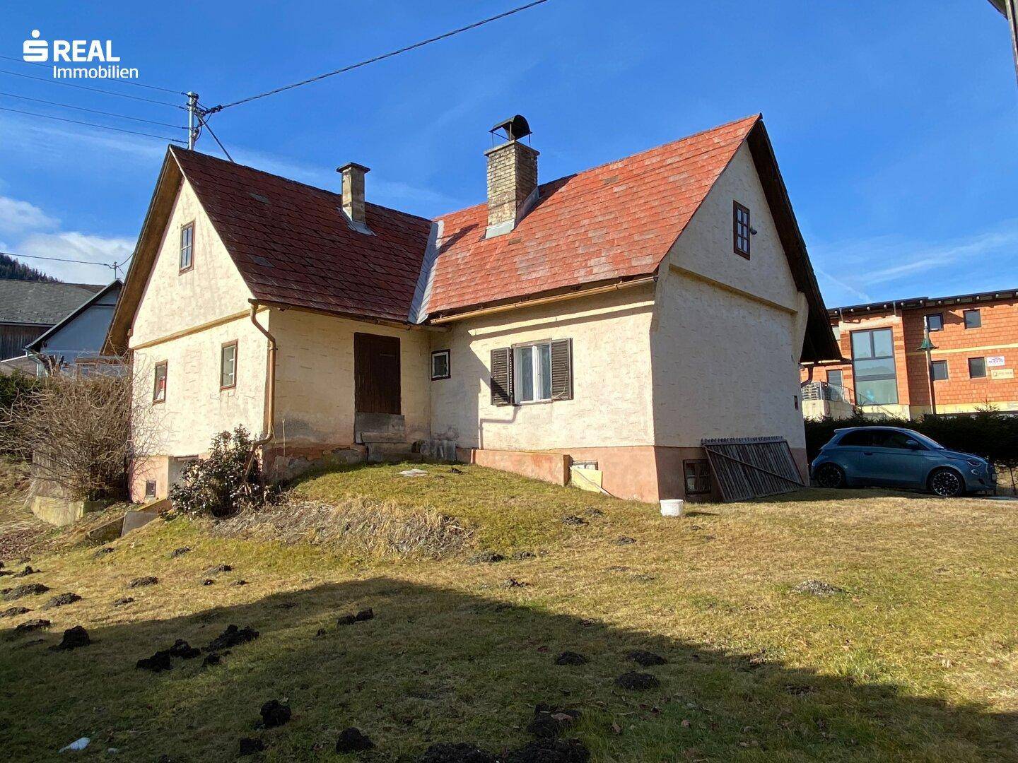 Seitenansicht des Landhauses mit rotem Dach, Schornstein und umliegender Rasenfläche.