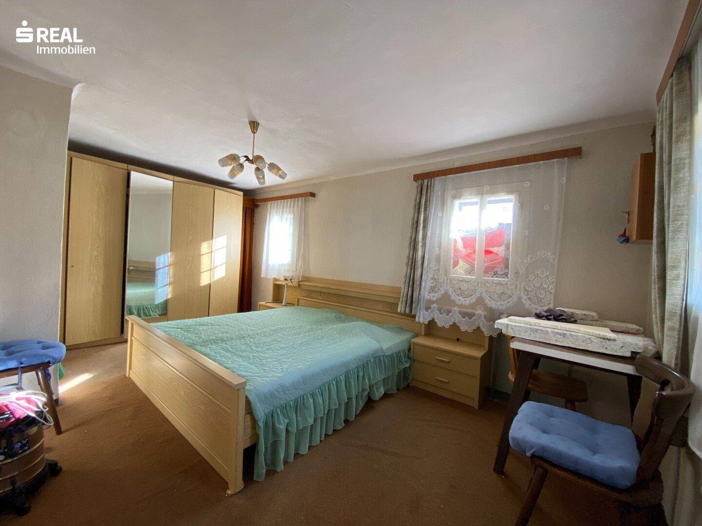Helles Schlafzimmer mit Doppelbett, Spiegelschrank und einfacher Einrichtung.