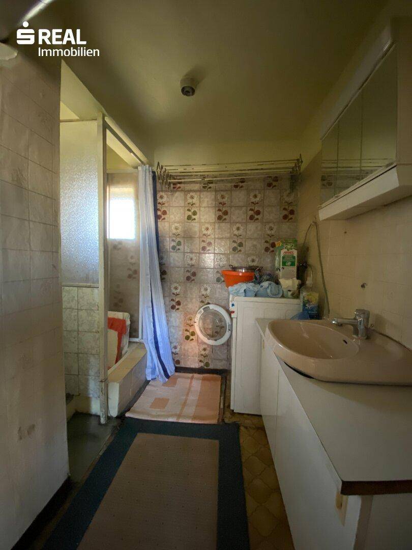 Funktionales Badezimmer mit Waschbecken, Waschmaschine und Duschbereich mit Fliesen.