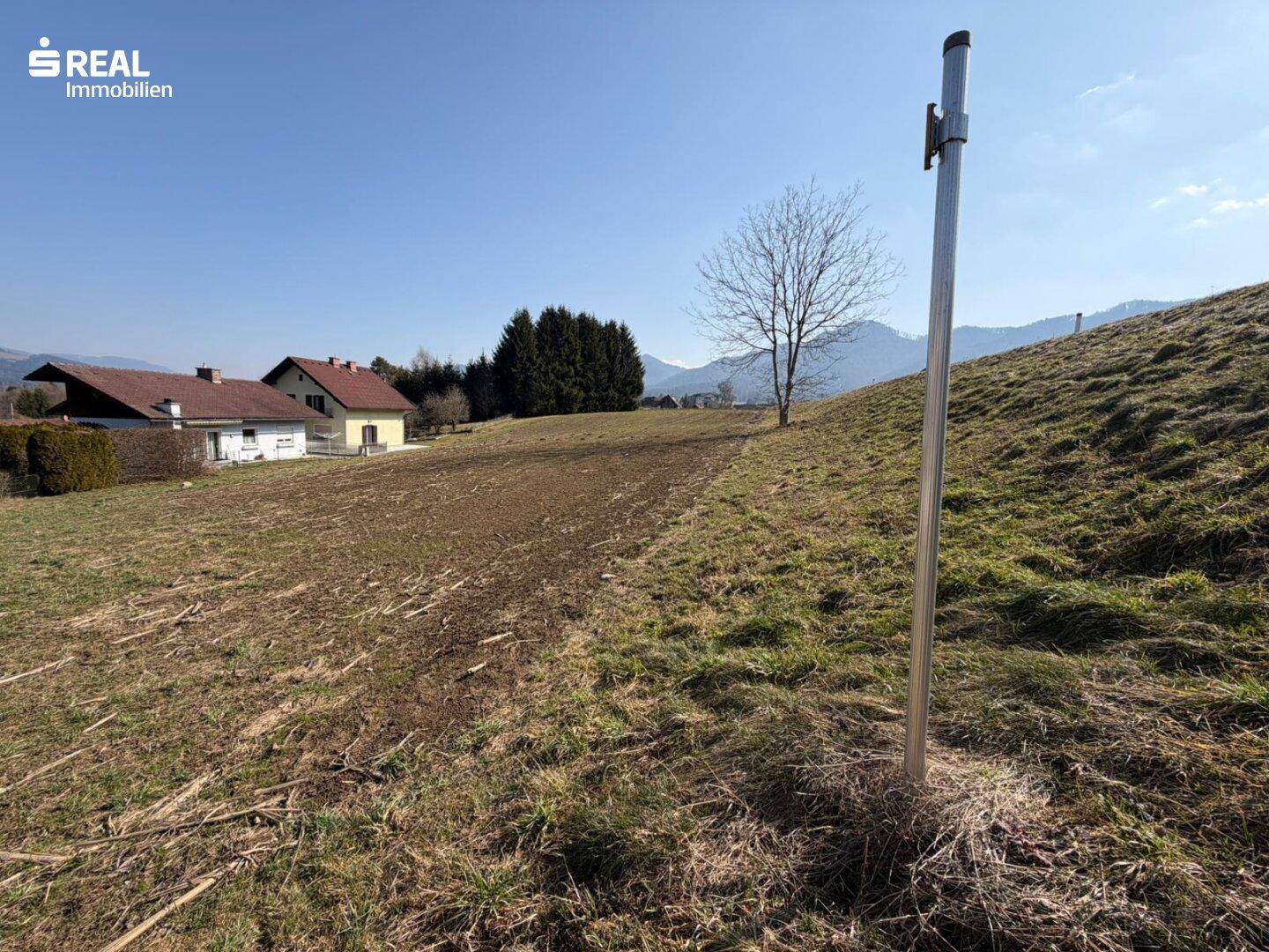 Hügeliges Grundstück mit freiem Blick auf die Bergkette und nahegelegene Wohnhäuser.