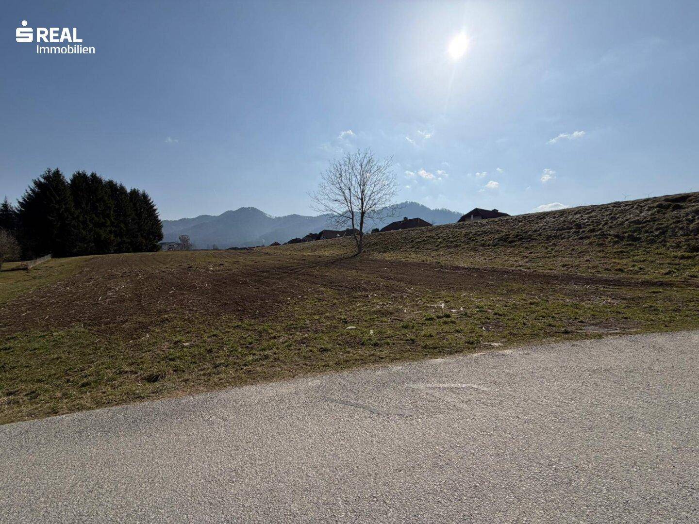 Sonniges Grundstück mit asphaltierter Zufahrt und Panoramablick auf die umliegenden Berge.