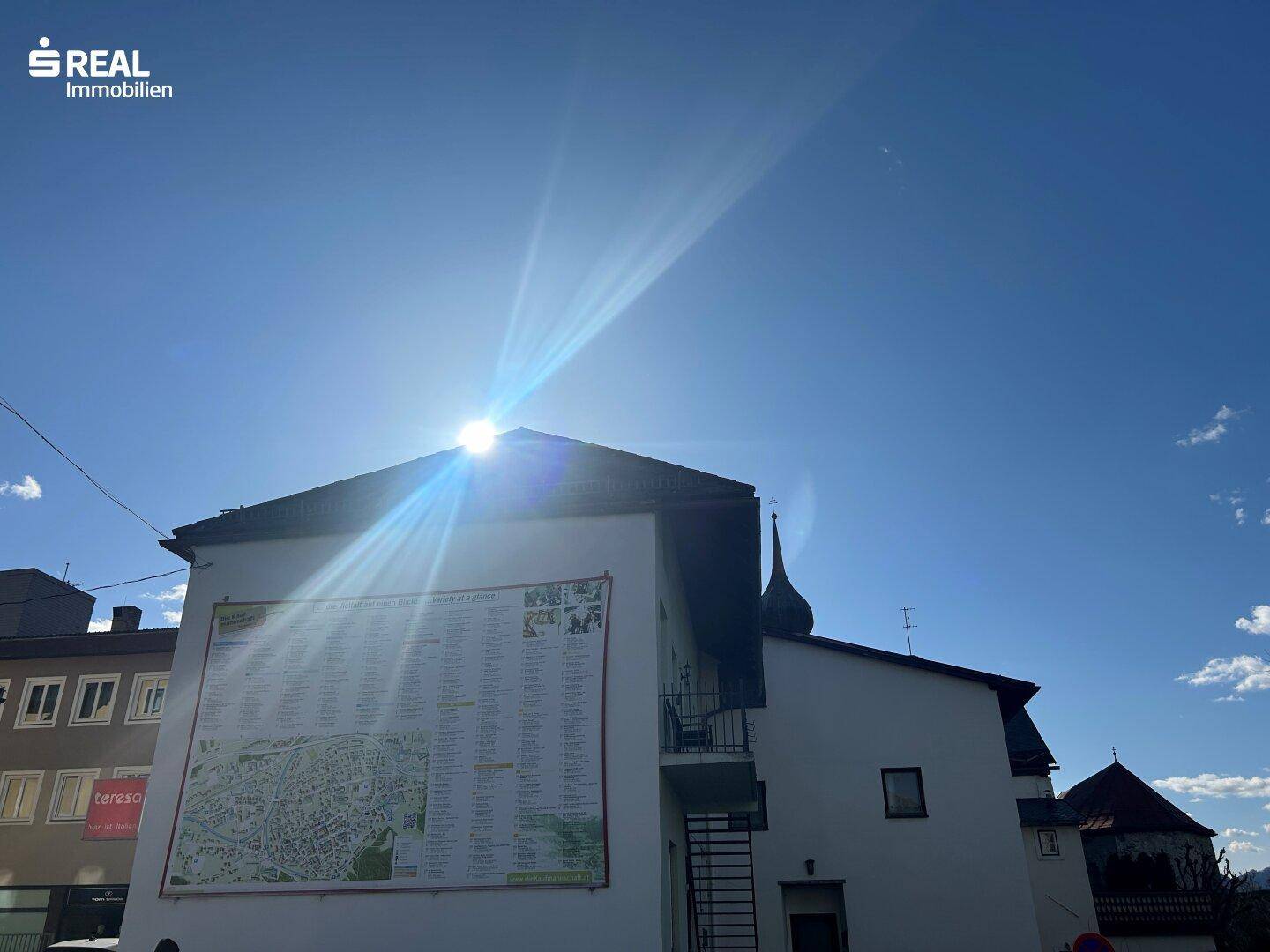 Rückansicht eines Gebäudes mit einer großen Stadtkarte an der Wand, überstrahlt von der Sonne.