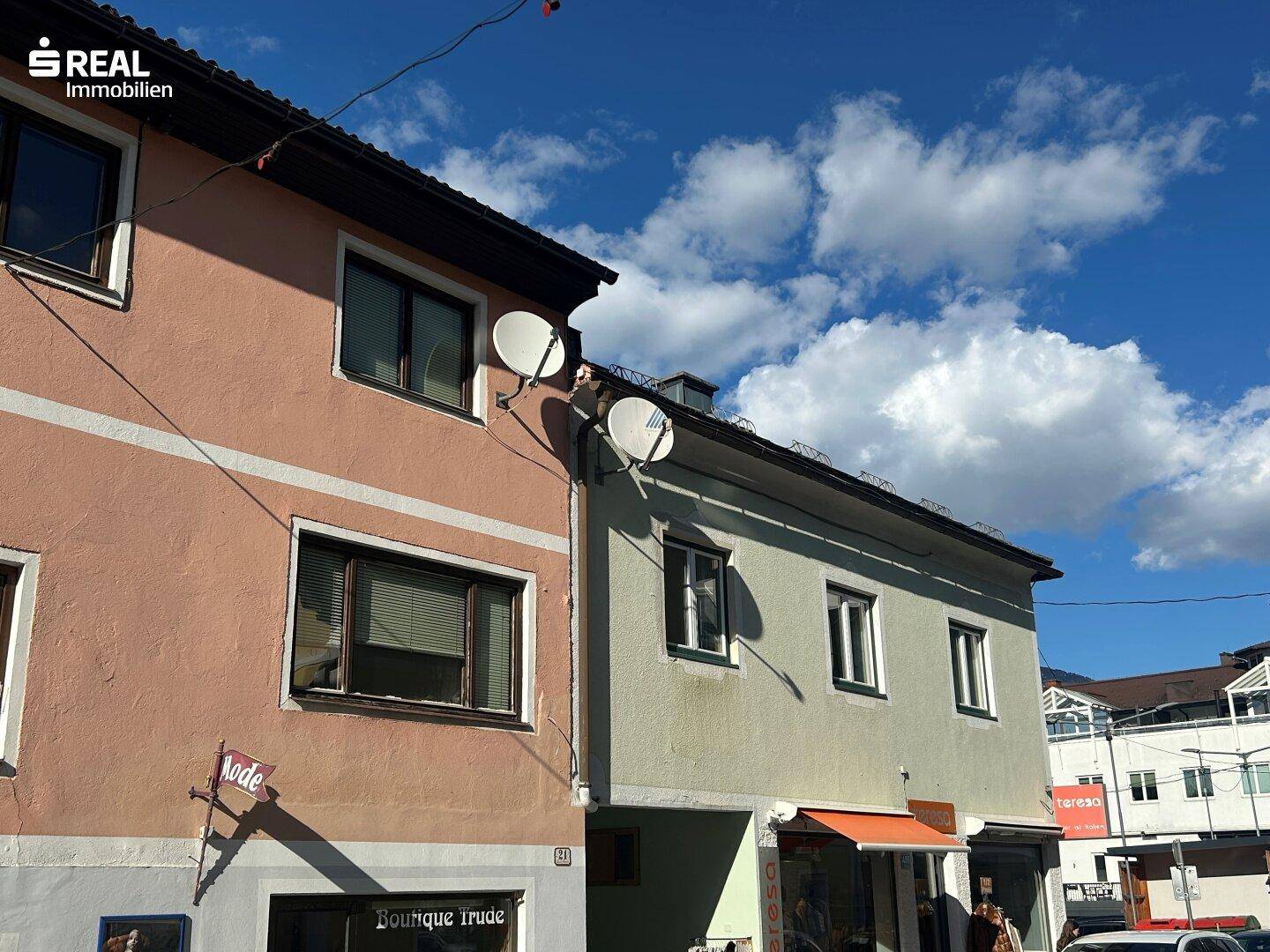 Nahaufnahme der Fassaden zweier Gebäude mit Satellitenschüsseln und Geschäften im Erdgeschoss.