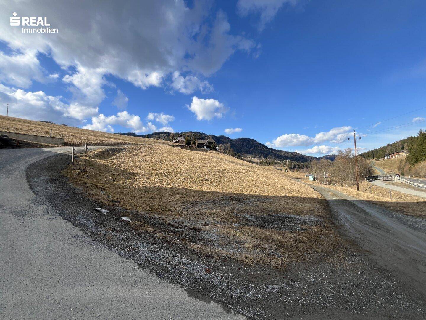 Kurvige Straße neben einer Wiese mit Blick auf entfernte Gebäude in einem Tal.