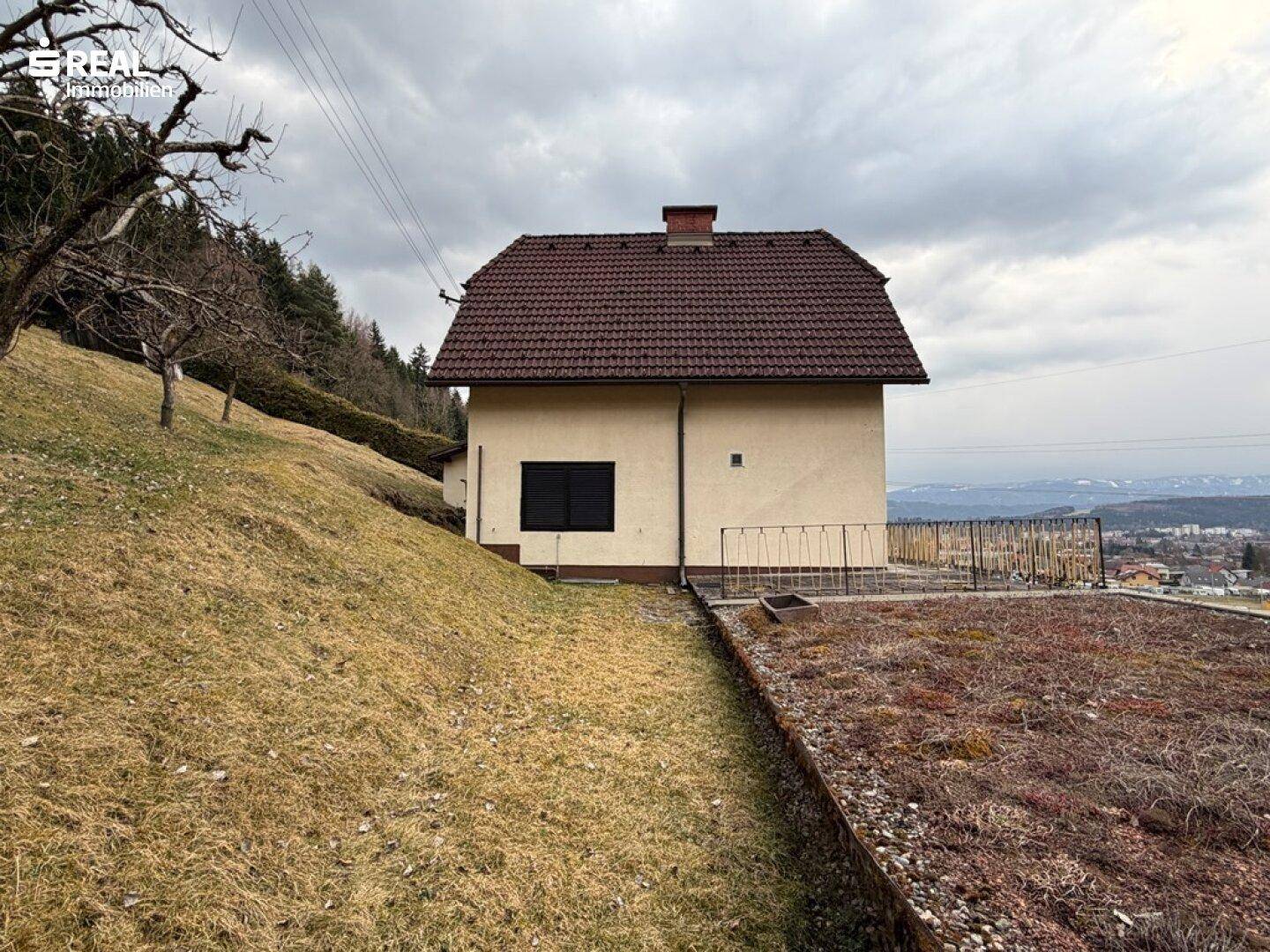 Seitenansicht des Hauses mit weitem Blick über die Landschaft und angrenzendem Hang.