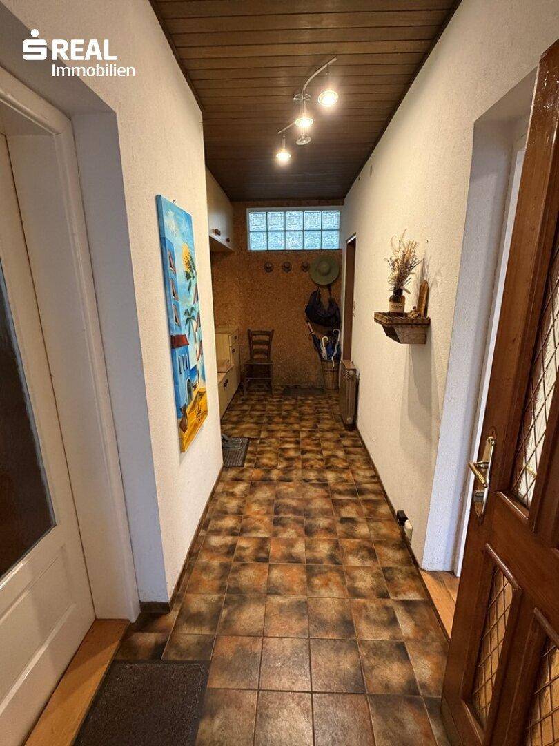Langer Flur mit rustikalen Fliesen und Holzdecke, der zu weiteren Räumen führt.