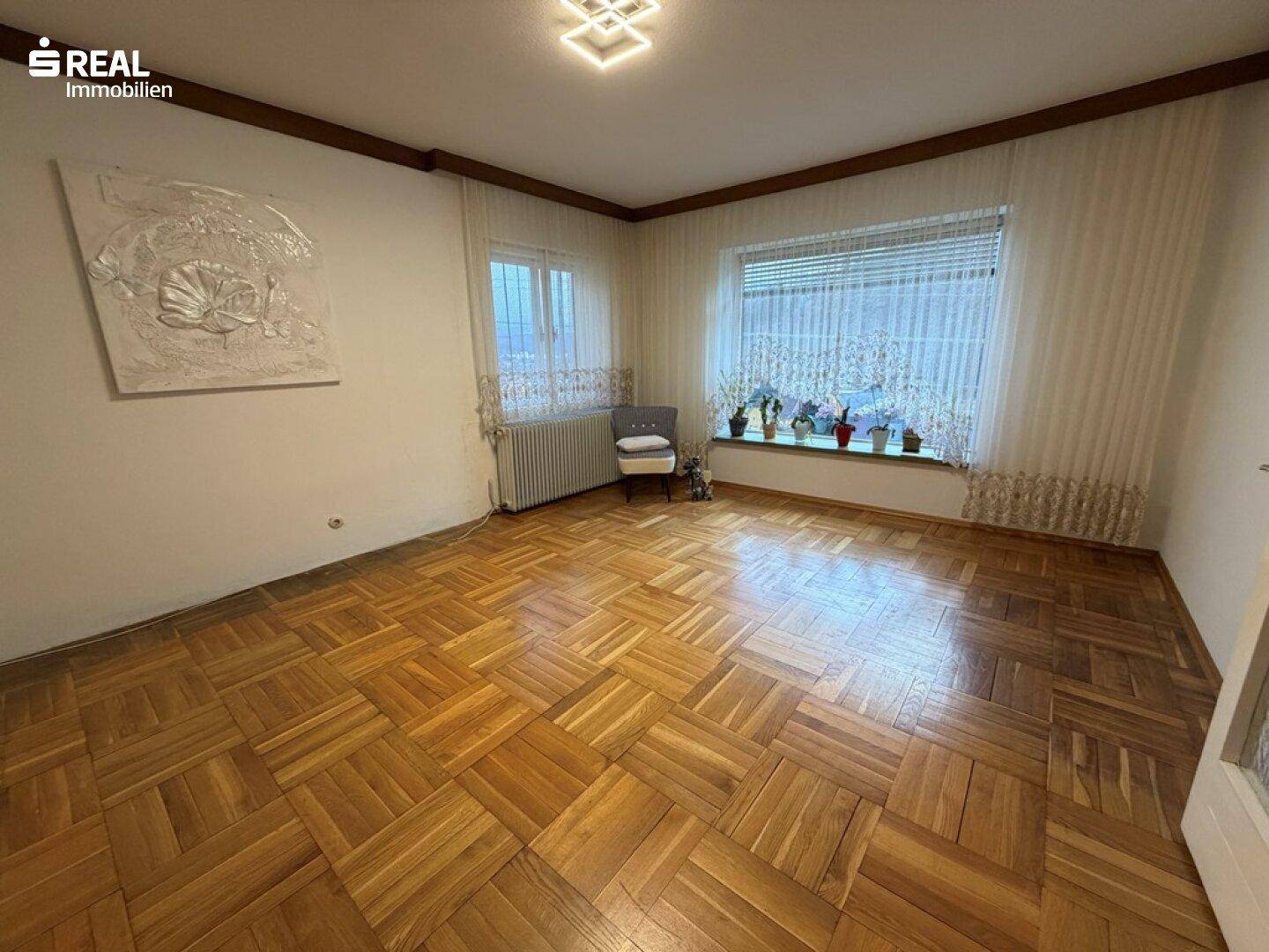 Geräumiges Wohnzimmer mit klassischem Parkettboden und großen Fenstern für viel Tageslicht.