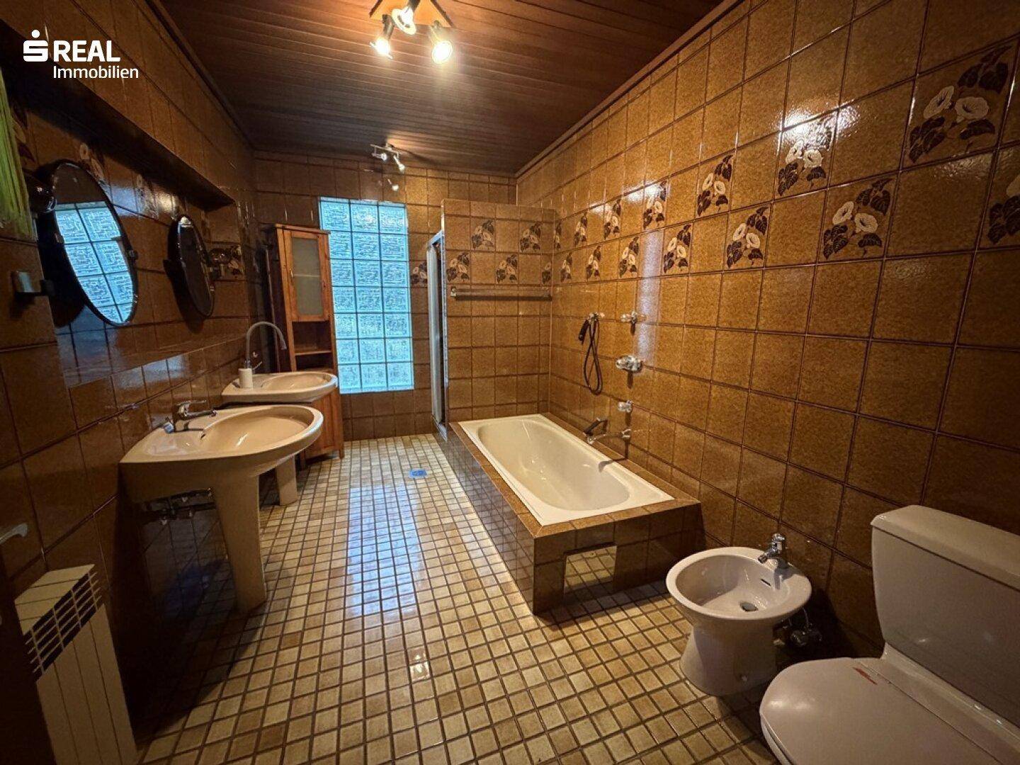 Badezimmer mit braunen Fliesen, zwei Waschbecken, Badewanne und Bidet in traditionellem Stil.