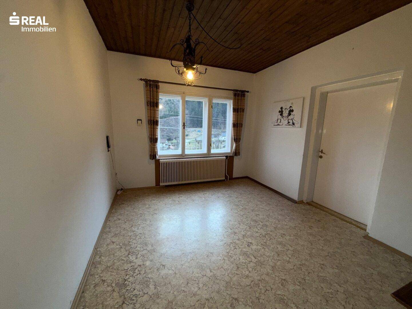 Esszimmer oder Mehrzweckraum mit Linoleumboden und Fensterblick ins Grüne.