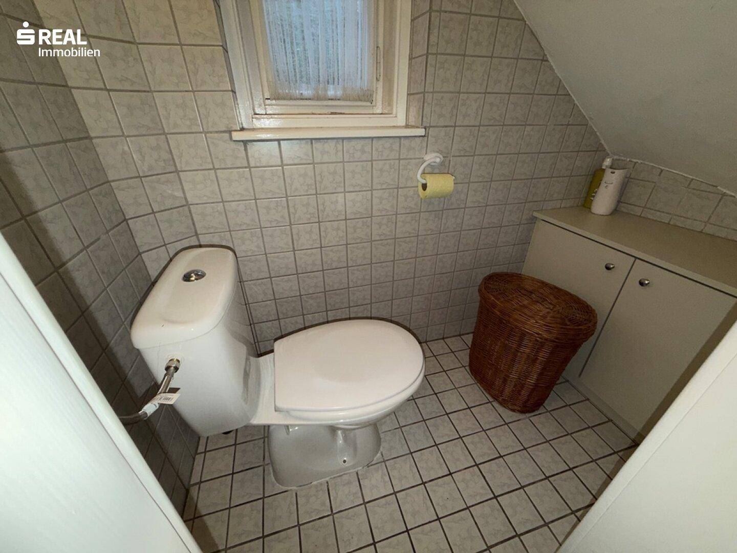 Kleines WC mit Fliesenboden und Fenster, ausgestattet mit einer Standardtoilette.