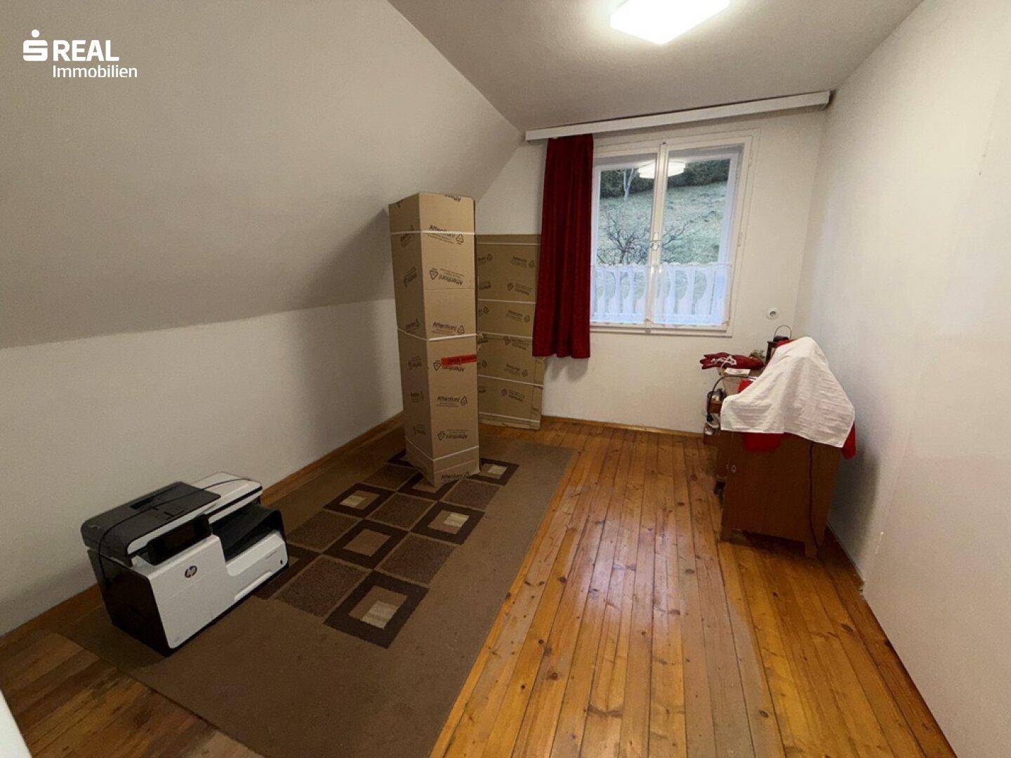 Dachzimmer mit Holzdielenboden und schrägen Wänden, bietet gemütlichen Wohnraum.