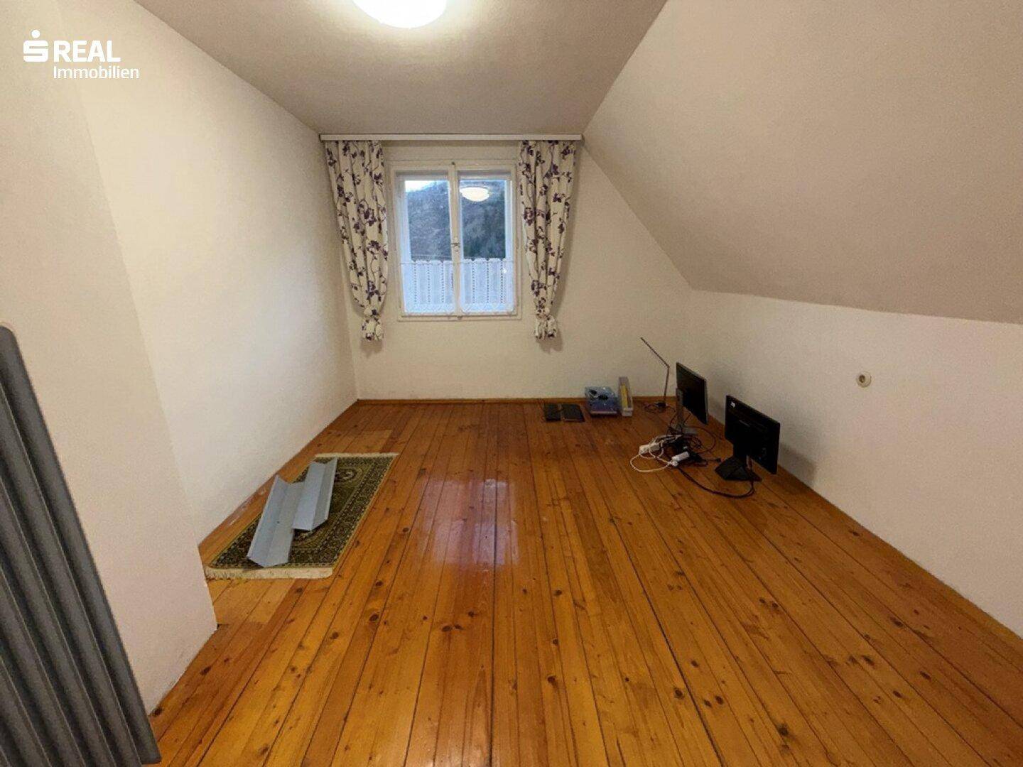 Dachzimmer mit Holzdielenboden und schrägen Wänden, ideal als Schlaf- oder Arbeitszimmer.