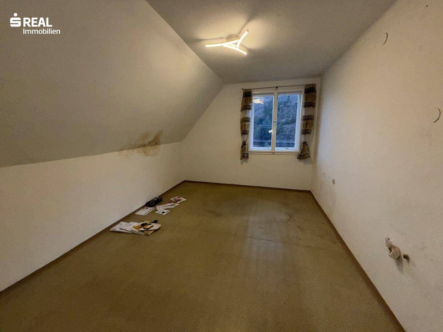 Dachzimmer mit schrägen Wänden und Teppichboden, bietet zusätzlichen Wohnraum.