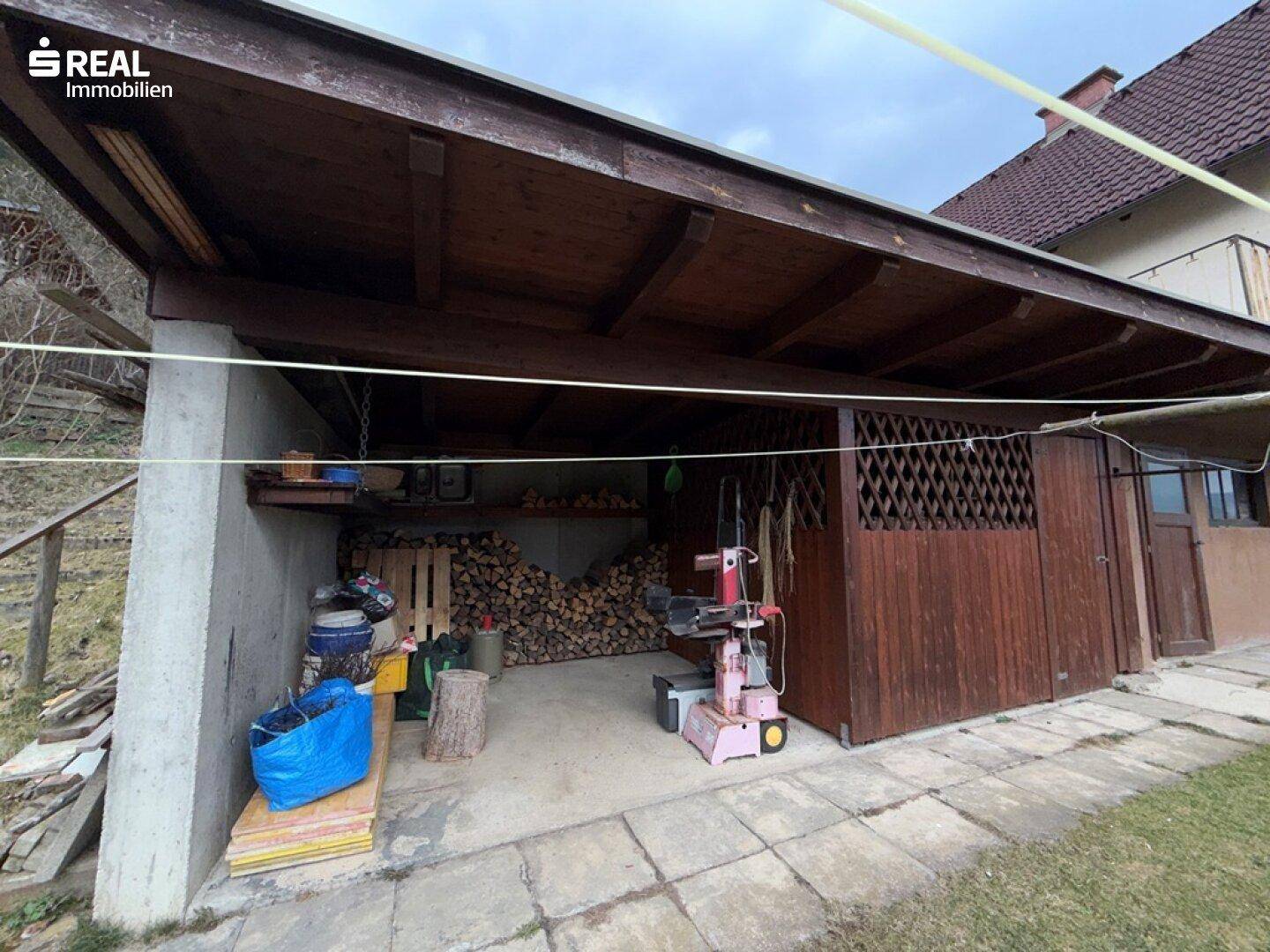 Überdachter Abstellbereich mit Holzstapel und Werkzeugen, ideal für Lagerung und Arbeiten.