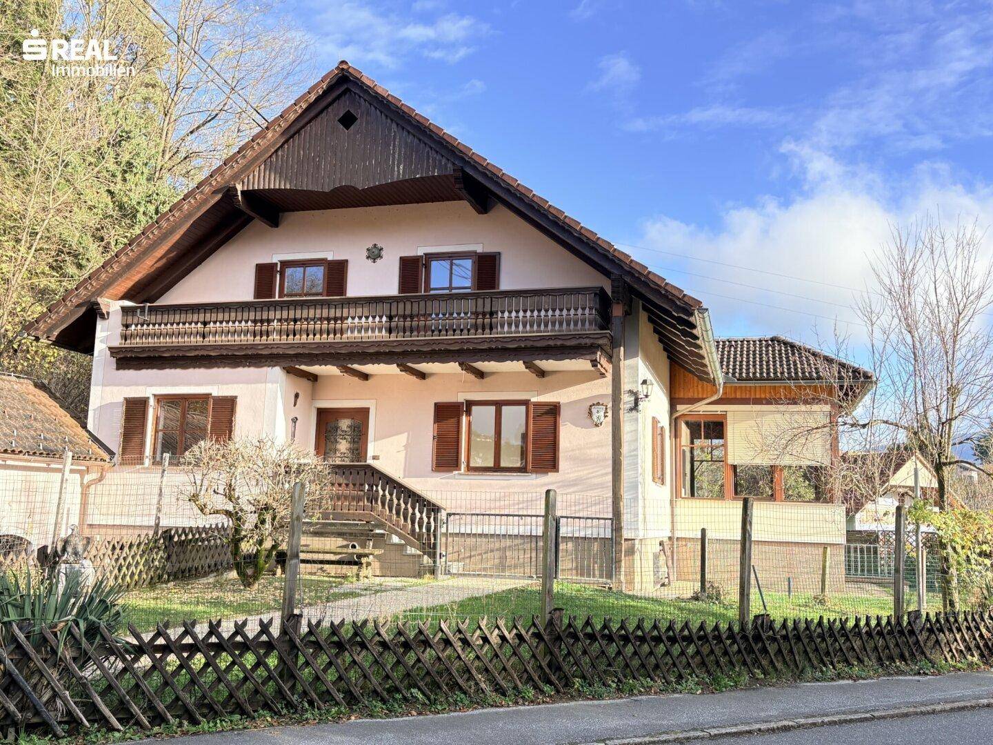 Wohnhaus mit traditioneller Architektur, Holzbalkon und gepflegtem Vorgarten.