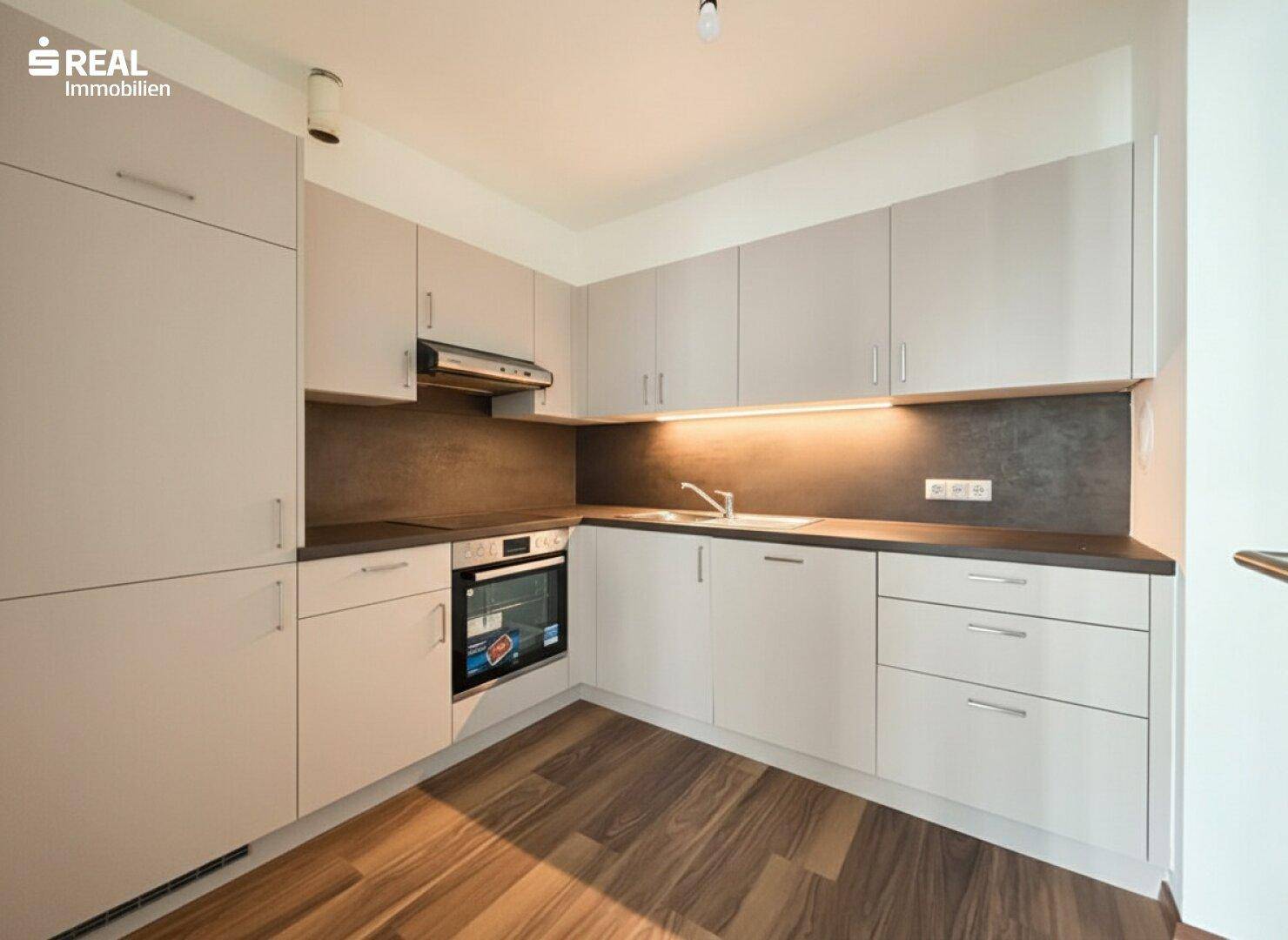 Moderne Einbauküche mit hellgrauen Schränken, dunkler Arbeitsplatte und integriertem Backofen.