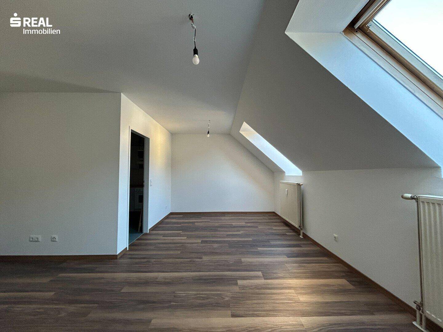 Helles Schlafzimmer im Dachgeschoss mit Laminatboden und Dachfenster.