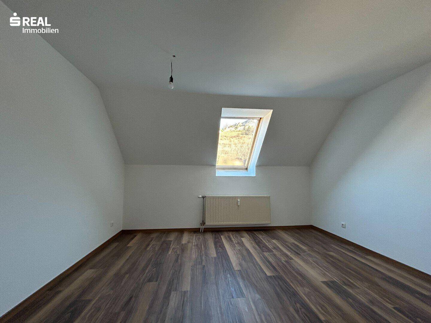 Geräumiges Schlafzimmer im Dachgeschoss mit Laminatboden und einem Dachfenster.