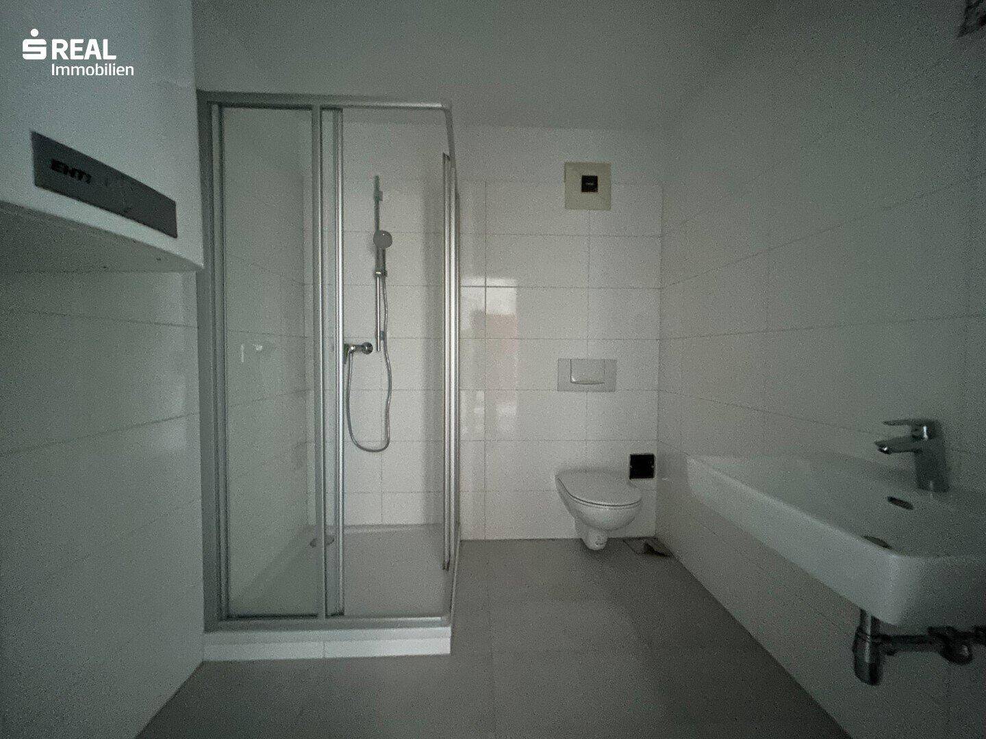 Modernisiertes Badezimmer mit Duschkabine, WC und Waschbecken in hellen Fliesen.