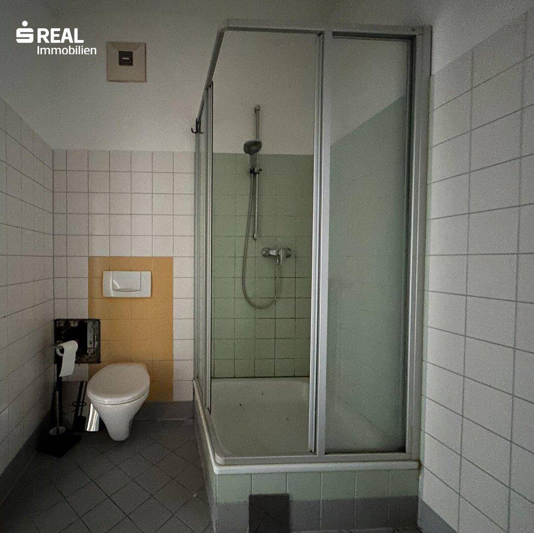 Badezimmer mit Duschkabine, WC und hellen Fliesen in einem älteren Stil.