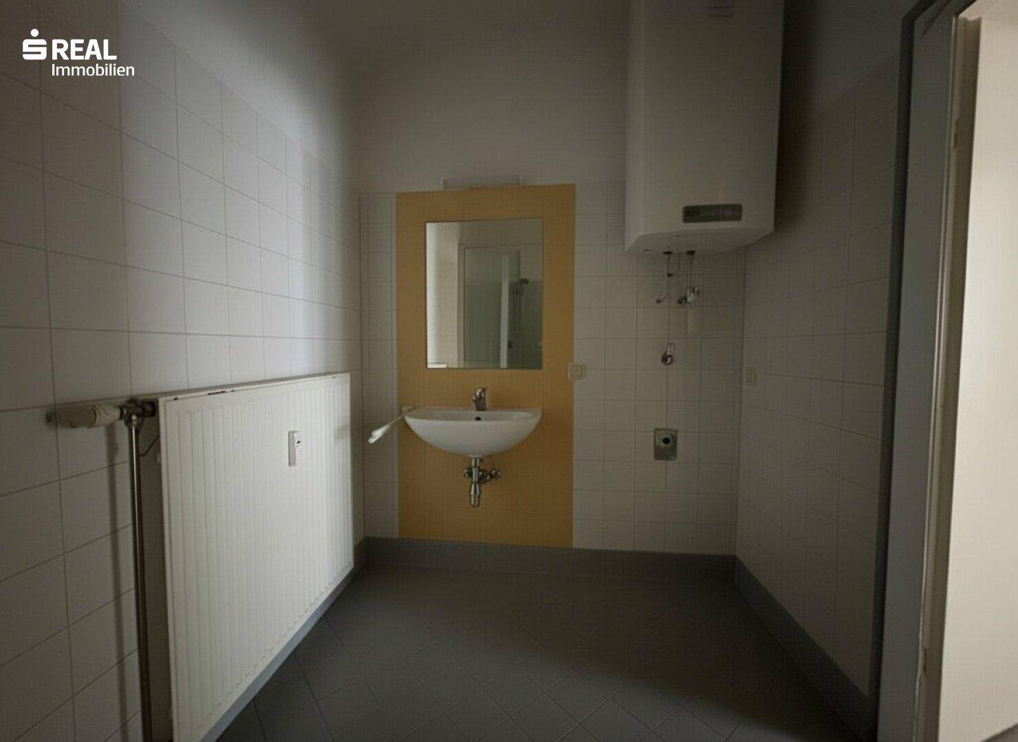 Badezimmer mit Waschbecken, Heizkörper und Fliesen in gelb-weißer Farbkombination.