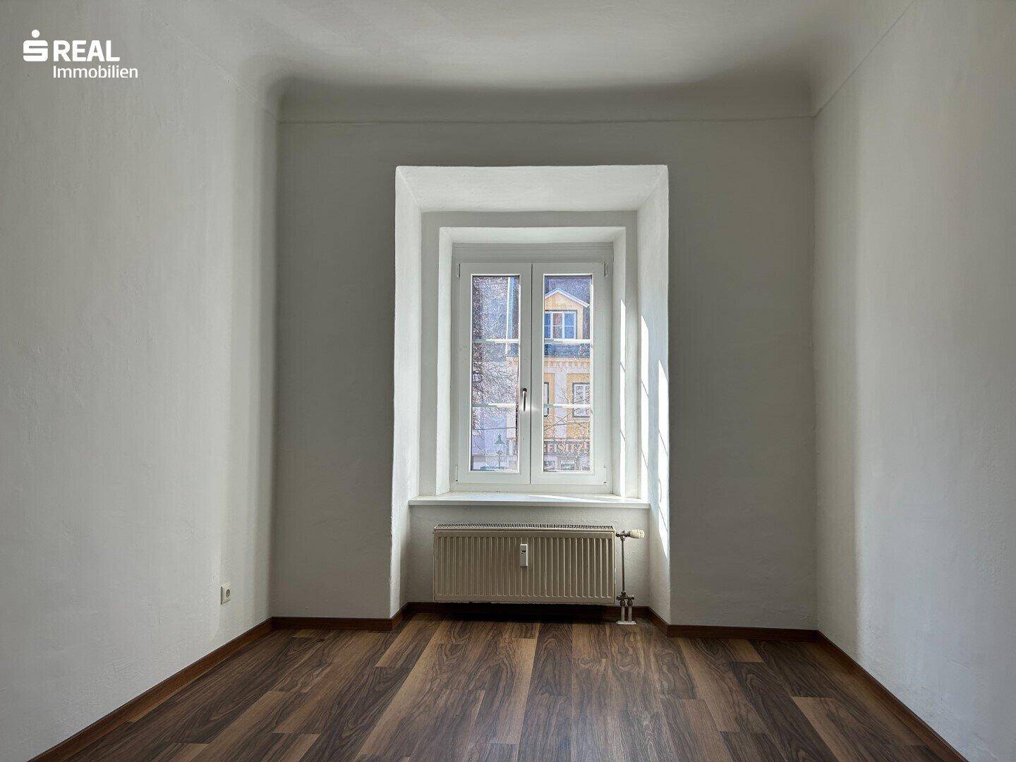Heller Raum mit einem großen Fenster und dunklem Laminatboden, ideal für Wohnzwecke.