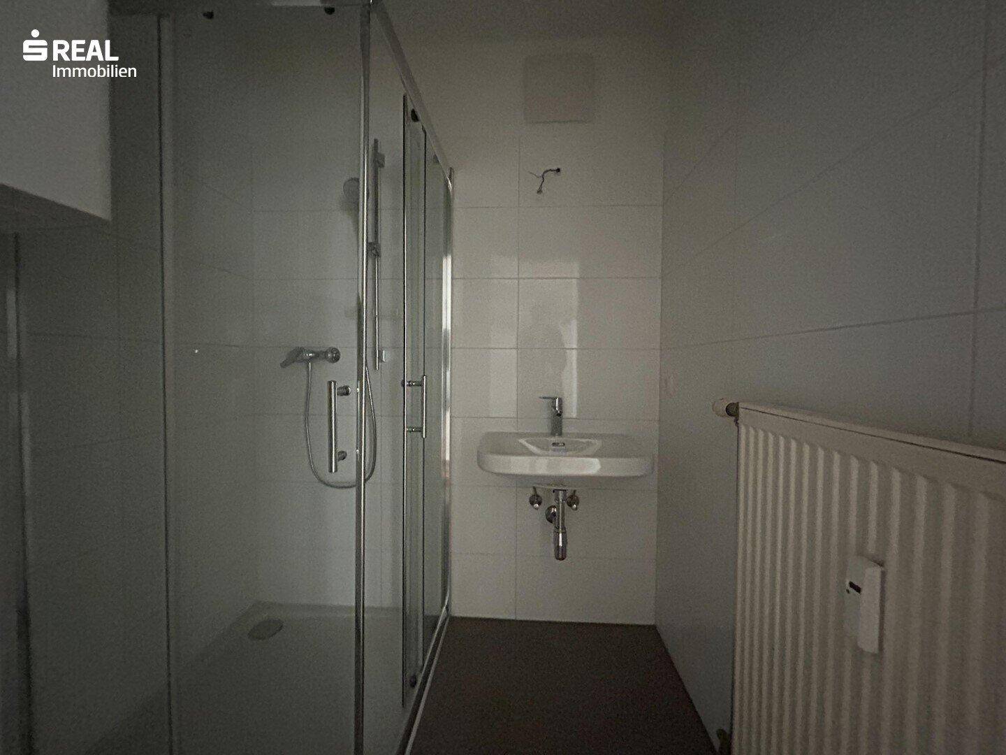 Badezimmer mit Duschkabine und Waschbecken, gefliest in neutralen Farben.