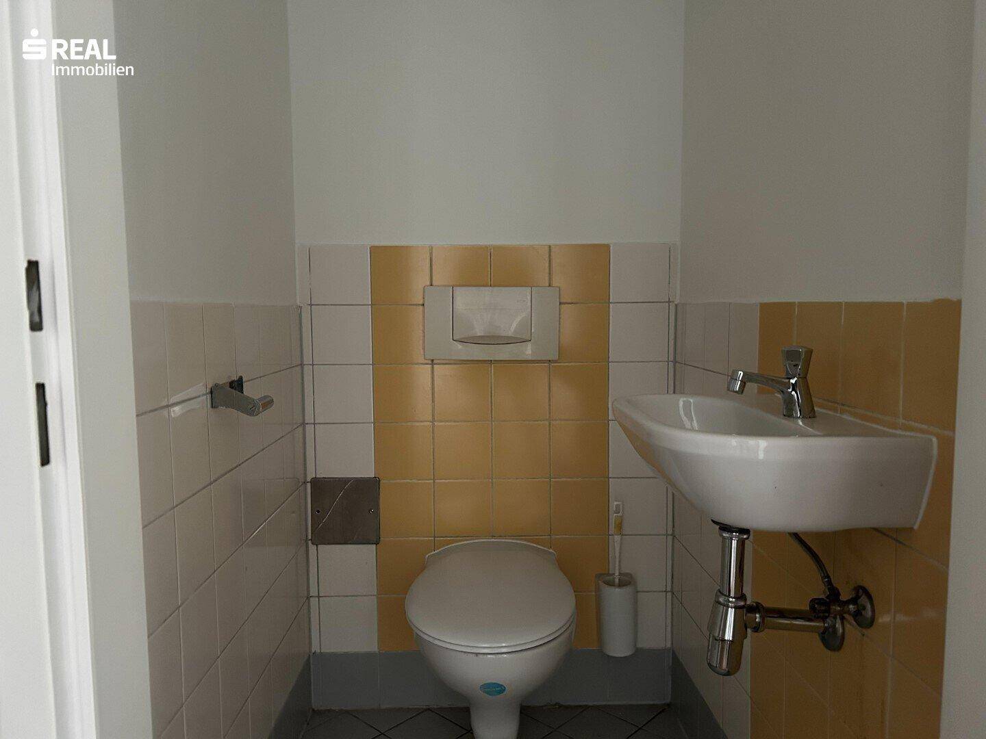 Separate Toilette mit Waschbecken und gelb-weißen Fliesen.