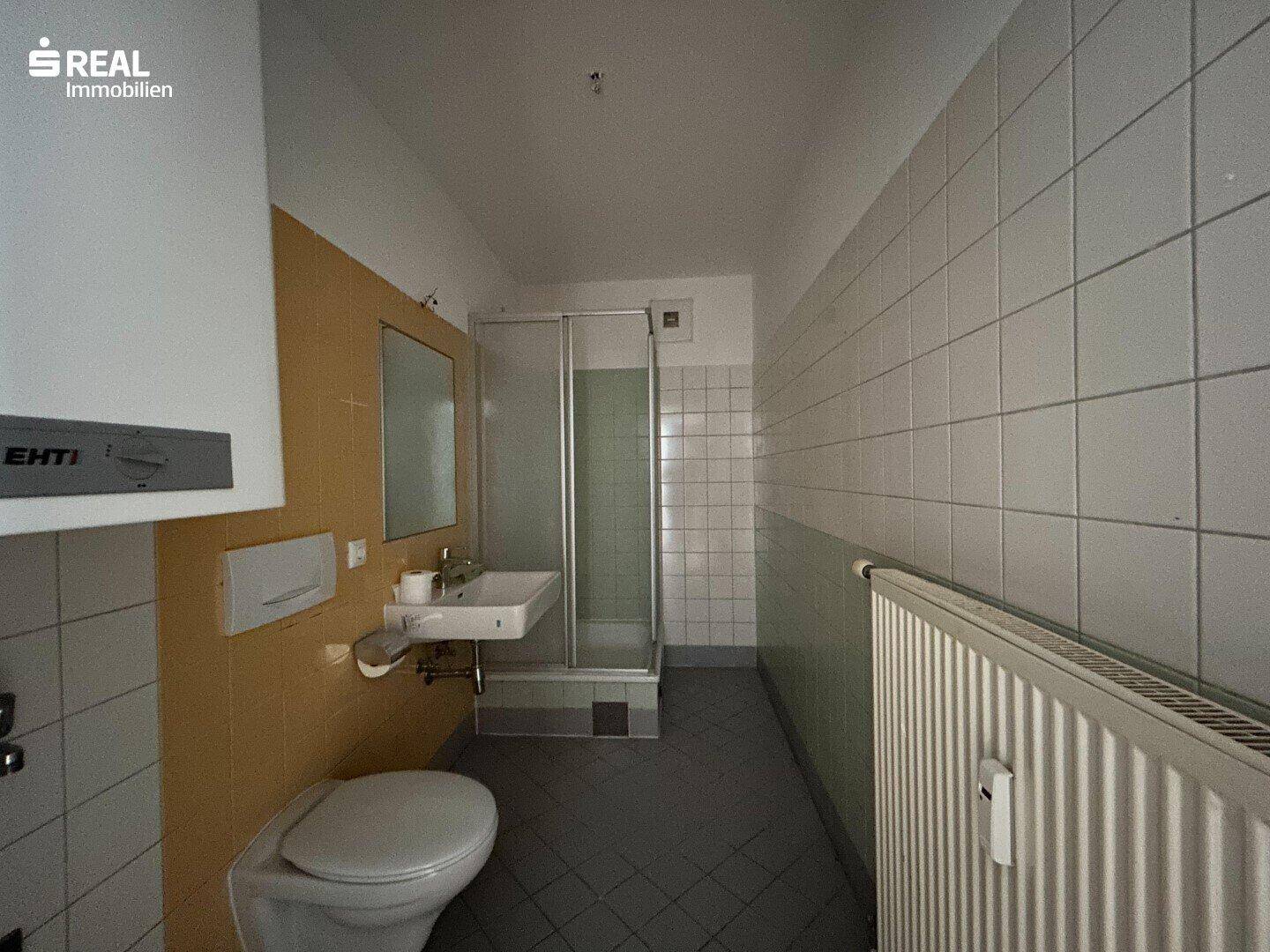 Badezimmer mit Duschkabine, WC und Waschbecken, gefliest in älterem Stil.