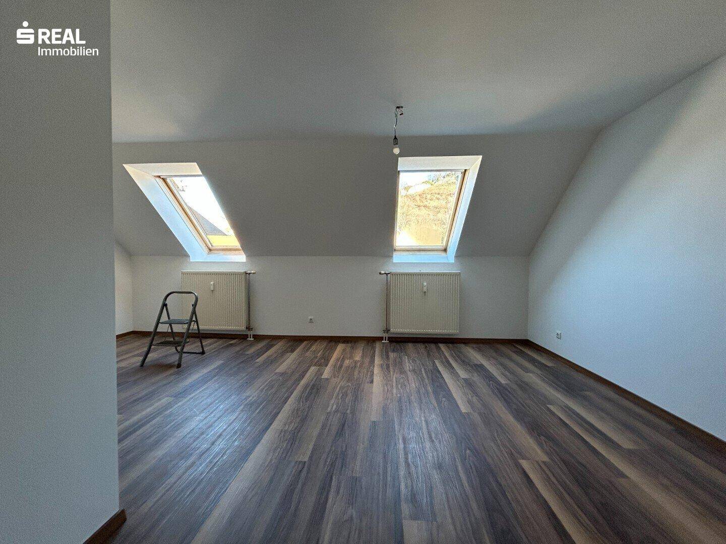 Helles Dachgeschosszimmer mit zwei Dachfenstern und Laminatboden.