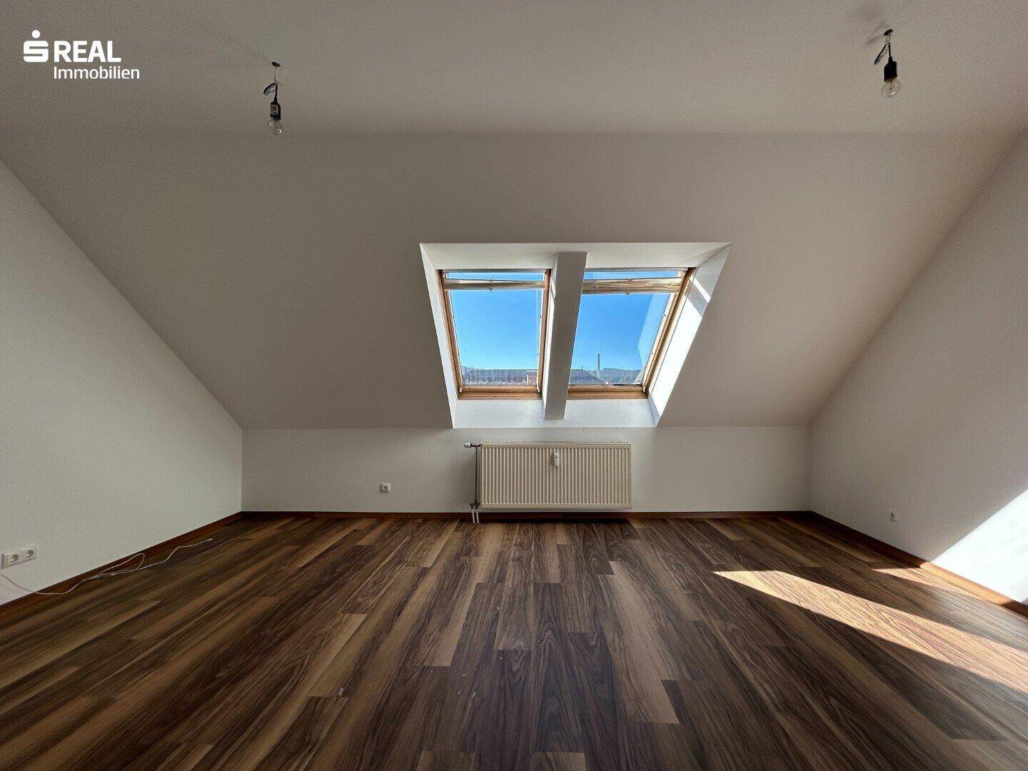 Geräumiger Dachbodenraum mit Laminatboden, schrägen Wänden und zwei Dachfenstern für viel Tageslicht.