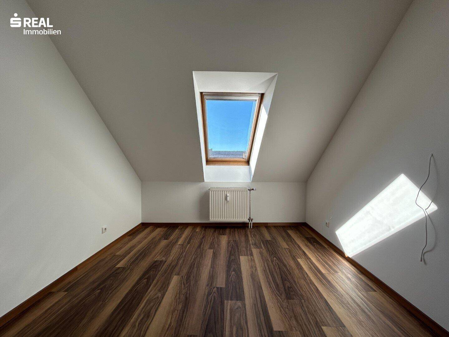 Heller Dachbodenraum mit einem einzelnen Dachfenster und Laminatboden, ideal für individuelle Gestaltung.