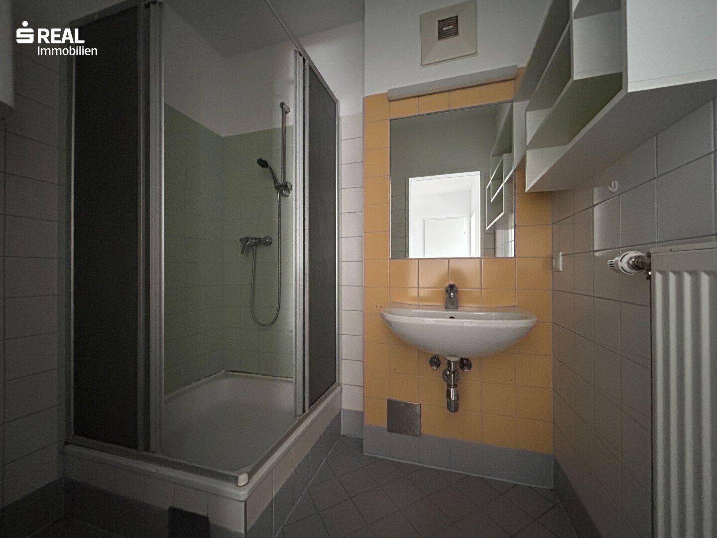 Badezimmer mit Duschkabine, Waschbecken und gelben Fliesen, das einen funktionalen Zustand aufweist.