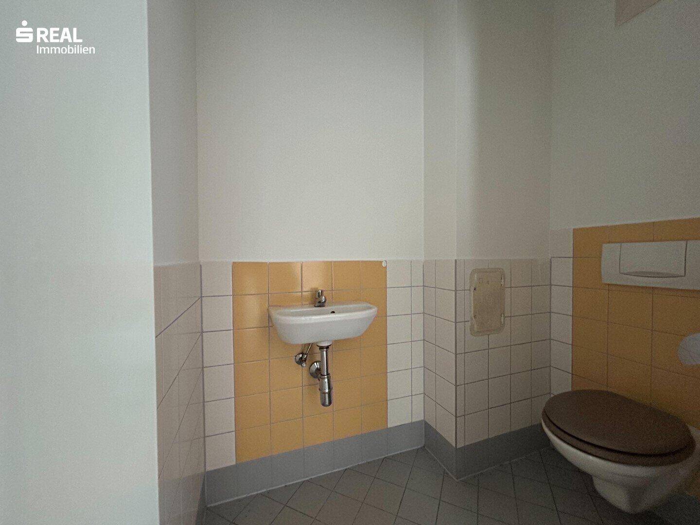 Separate Toilette mit Waschbecken und gelben Wandfliesen, in einem gepflegten, funktionalen Zustand.
