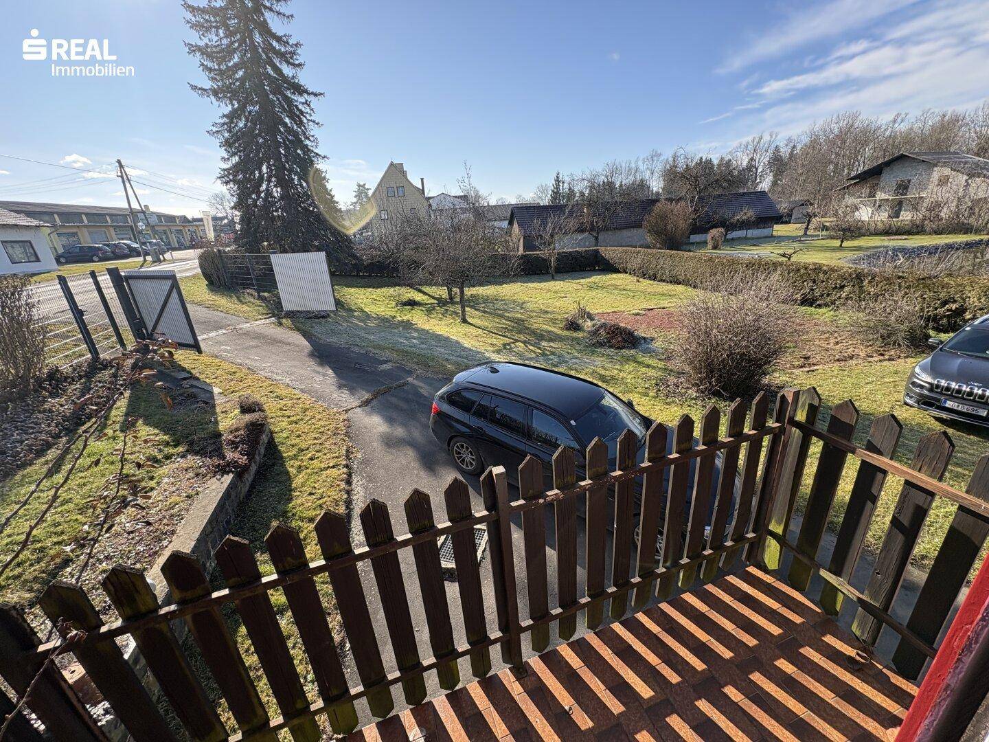 Kleiner Balkon mit Holzgeländer und Blick auf die Einfahrt und die grüne Umgebung.